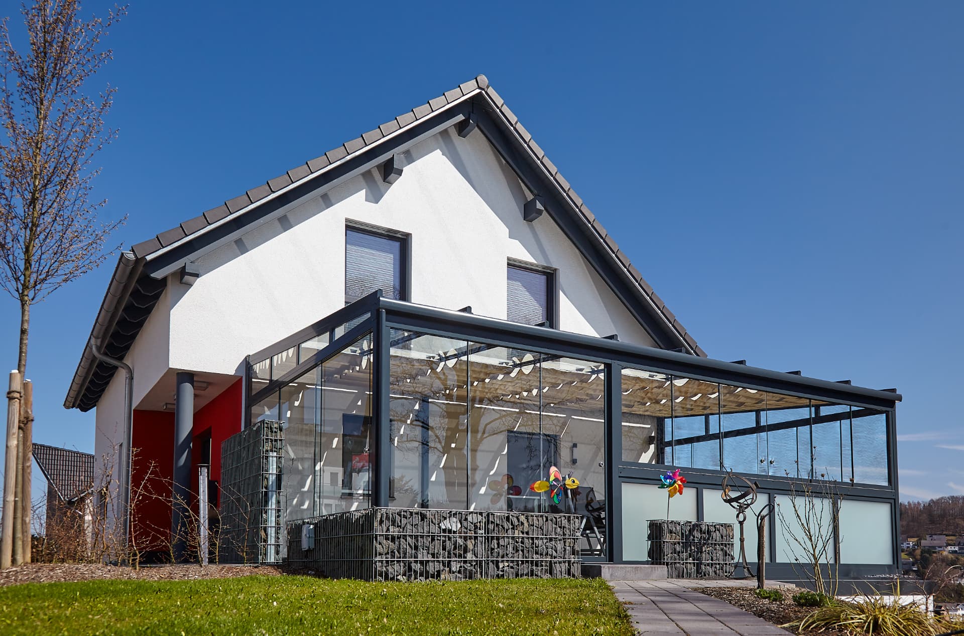 Großflächige Glas-Terrassenüberdachung mit anthrazitfarbenem Gestell und integriertem Sonnenschutz an einem Giebelhaus