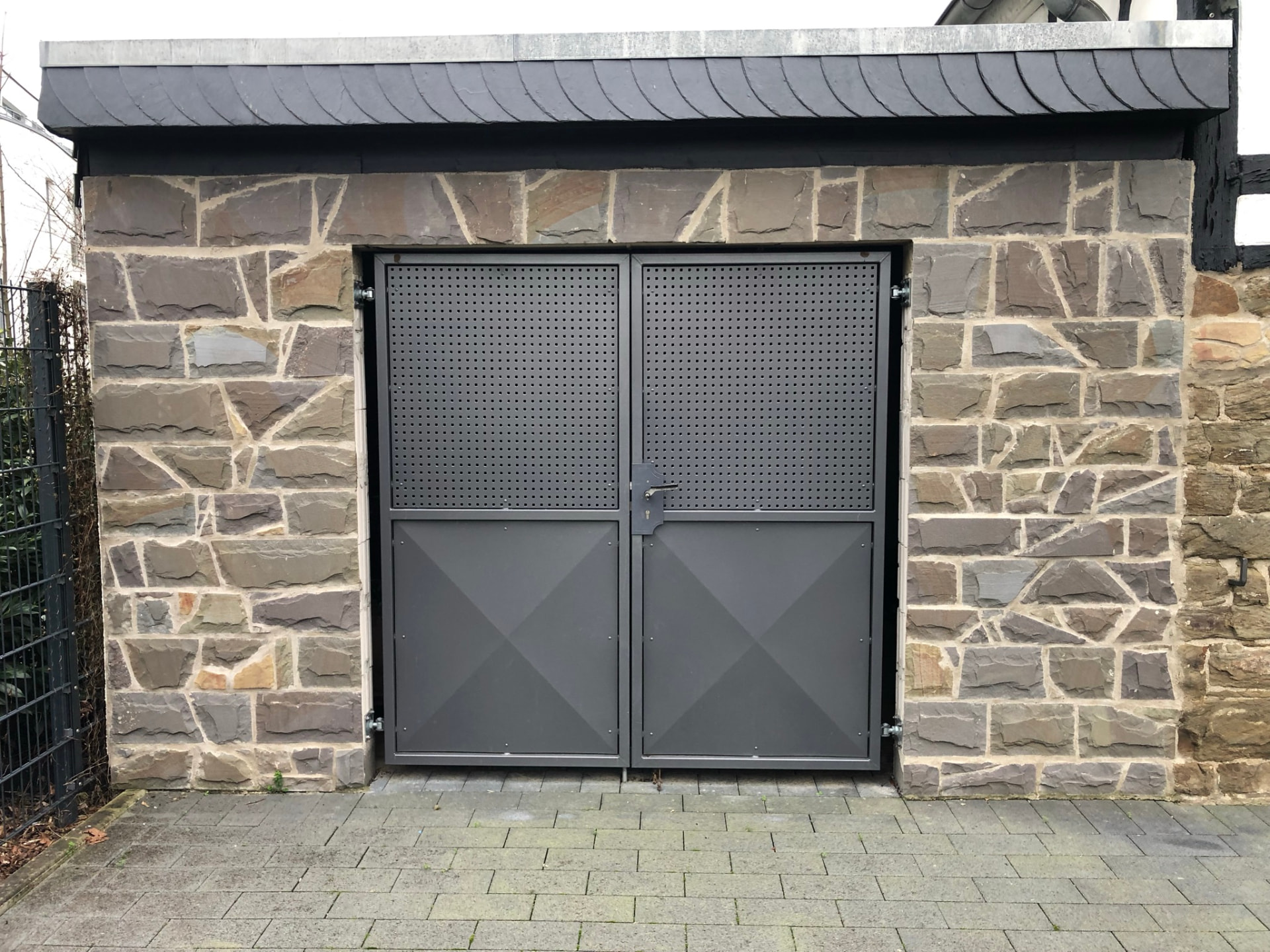 Zweiflügelige Stahltür mit Lochblech und Kreuzprägung in einer Natursteinwand