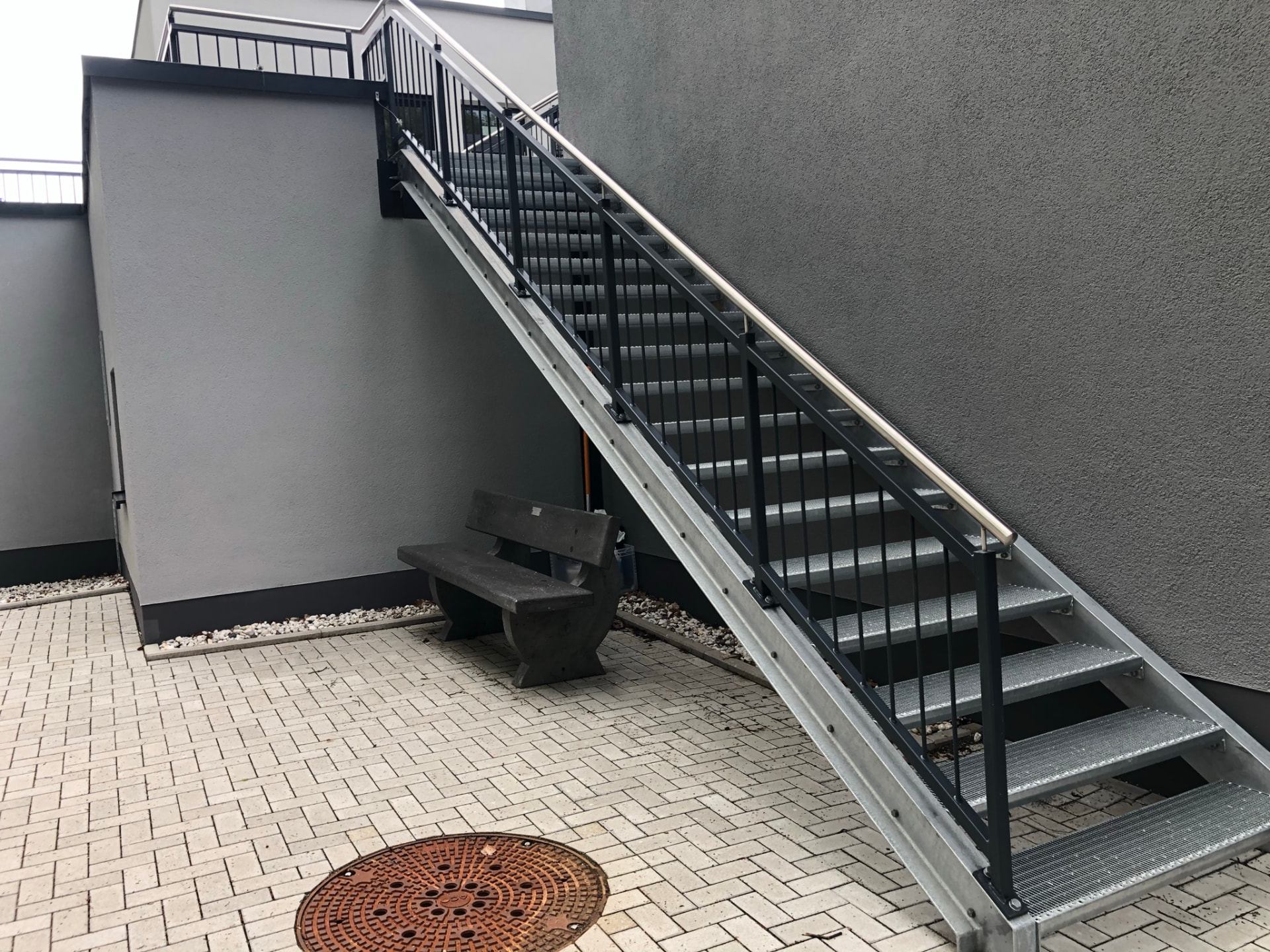 Außentreppe aus verzinktem Stahl mit dunklem Geländer und Edelstahlhandlauf entlang der Hauswand